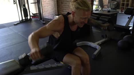 tattoo man muscles in home gym doing seated dumbbell shoulder lateral raise