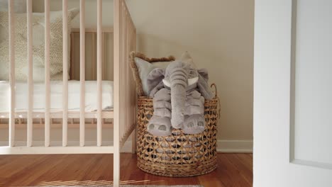 a stuffed animal elephant inside of a basket next to an infant's crib