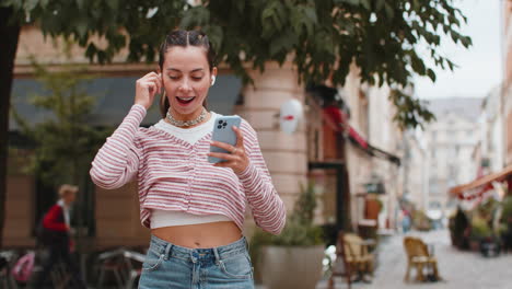 happy relaxed woman standing on city street in wireless earphones listening dancing music outdoors