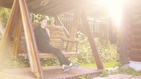 travelling young pretty girl swinging on a wooden swing near the summer house on vacation