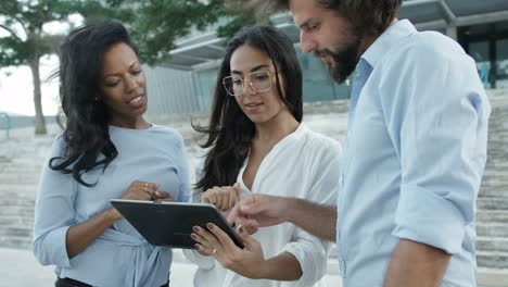 three colleagues standing outside watching at tablet outdoors