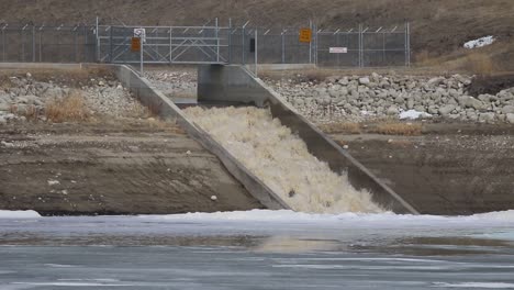 turbulent and dirty spring runoff over weir and into a partially frozen reservoir in the grassland region of alberta 001