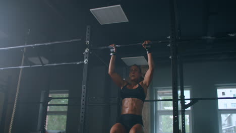 female athlete swinging on chin up bar. strong women doing chin-ups on gymnastic bars in gym. professional athlete does chin-up power strength and cross fitness exercises and everyday workout routine.