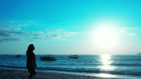 Mujer-Joven-Viendo-Una-Hermosa-Puesta-De-Sol-Con-Un-Sol-Brillante-Que-Se-Refleja-En-La-Superficie-Del-Mar-En-Calma,-Siluetas-De-Barcos-De-Pesca-Anclados,-Bali