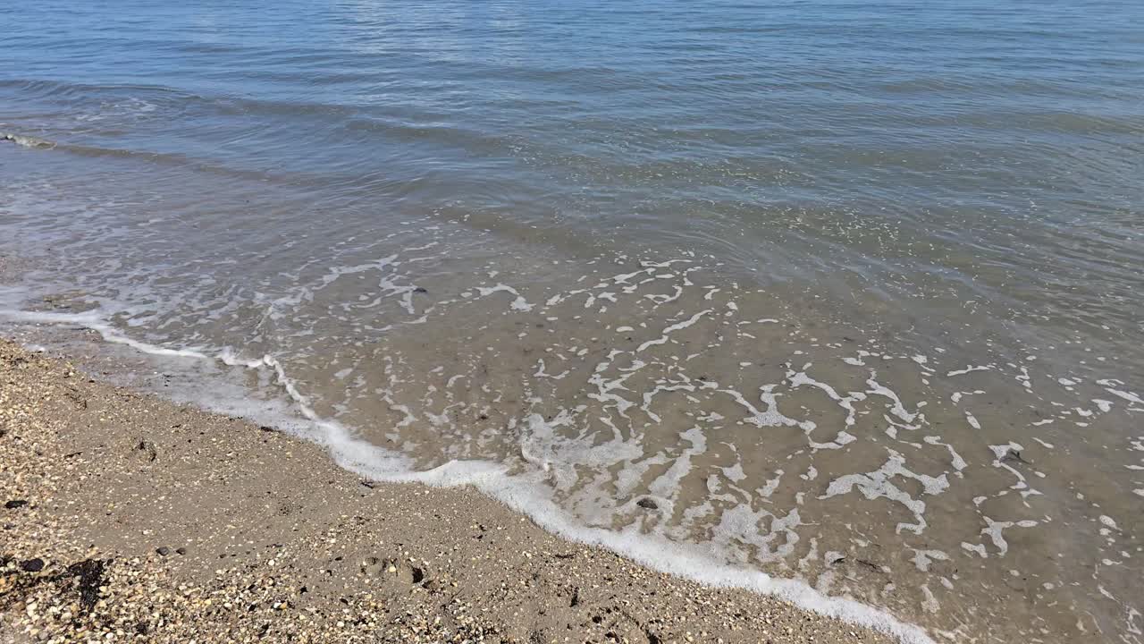Slow motion soft sea waves rolling on golden sandy beach at a sunny day
