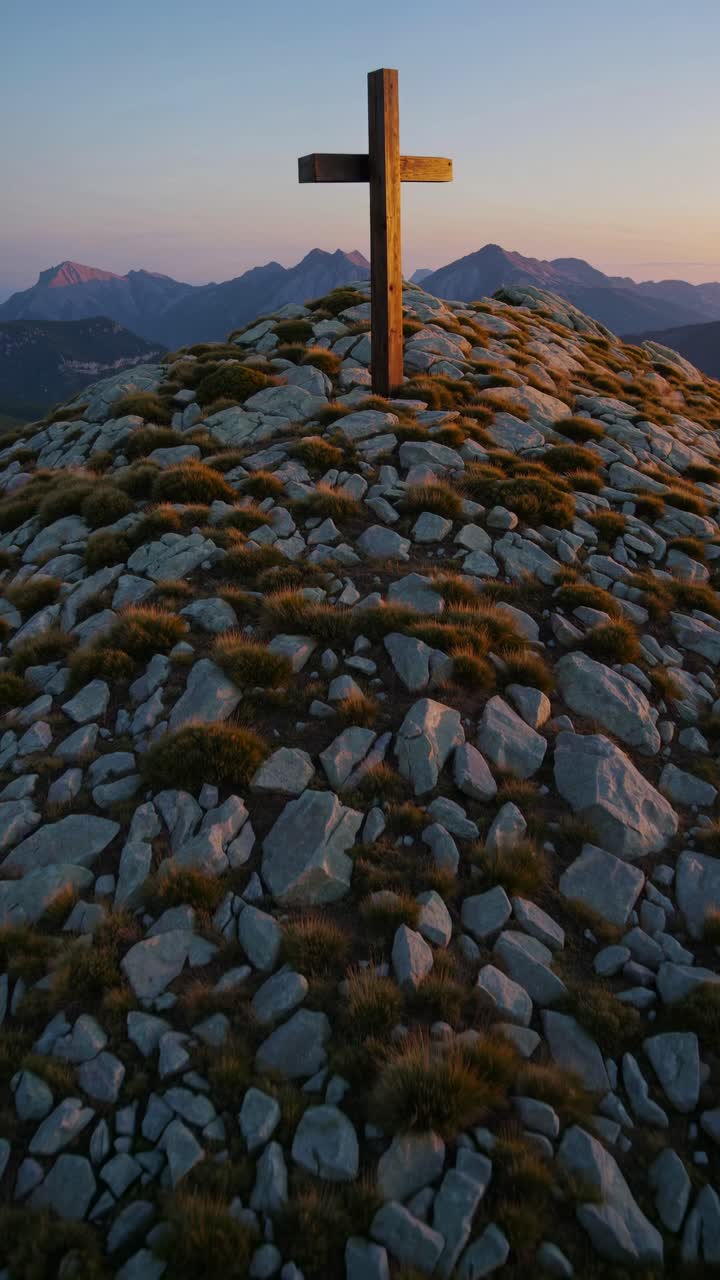 Aerial video shot of a wooden cross atop a rocky mountain peak at sunset, capturing serene