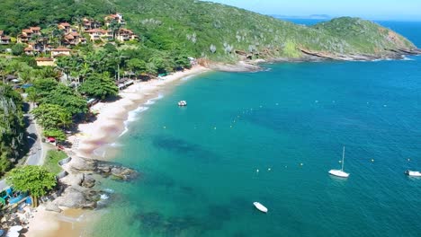 Aerial-of-calm-sea-waves-hitting-the-beautiful-beach-with-tall-green-cliffs-on-a-bright-sunny-day