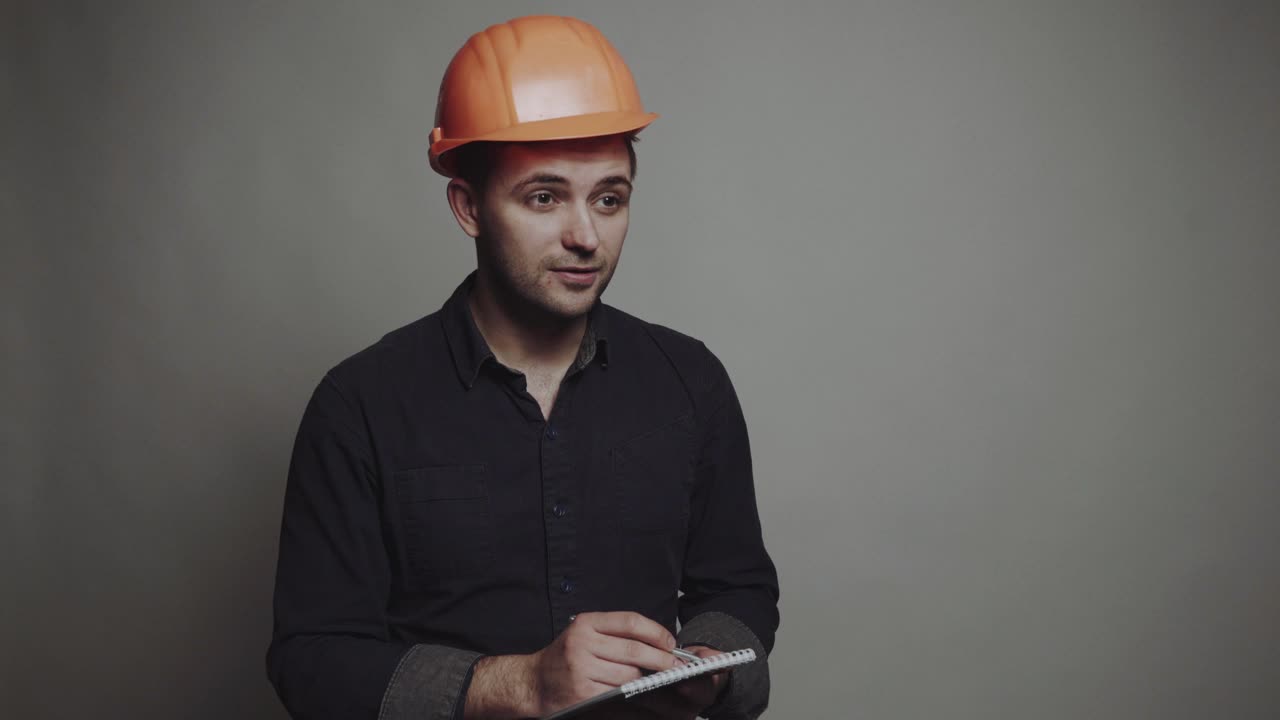 Young man architect in building helmet. Smiling young man architect in building helmet standing and writing on clipboard