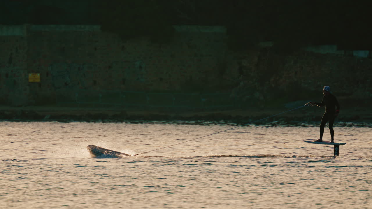 Silhouette di una persona che guida una tavola da surf elettrica sull'acqua calma del mare durante l'ora d'oro