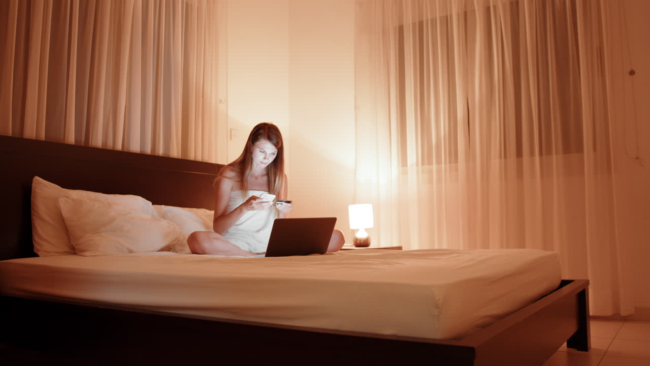 밤에 침대에서 노트북과 전화를 사용하는 여성