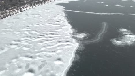 Vista-Aérea-Del-Agua-Parcialmente-Congelada,-Formaciones-De-Hielo-En-La-Orilla-Con-Nieve-Que-Cubre