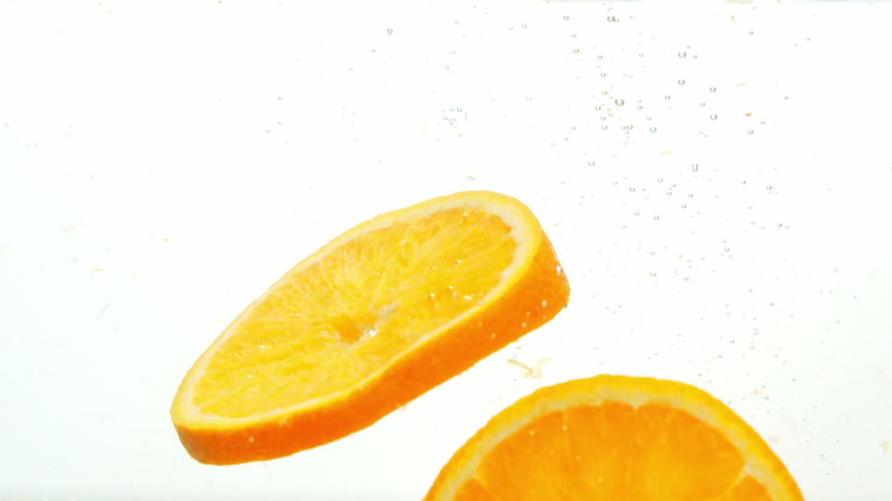 즙이 많은 오렌지 조각이 물에 떨어지고 기포가 떠오르고 떠 있습니다.