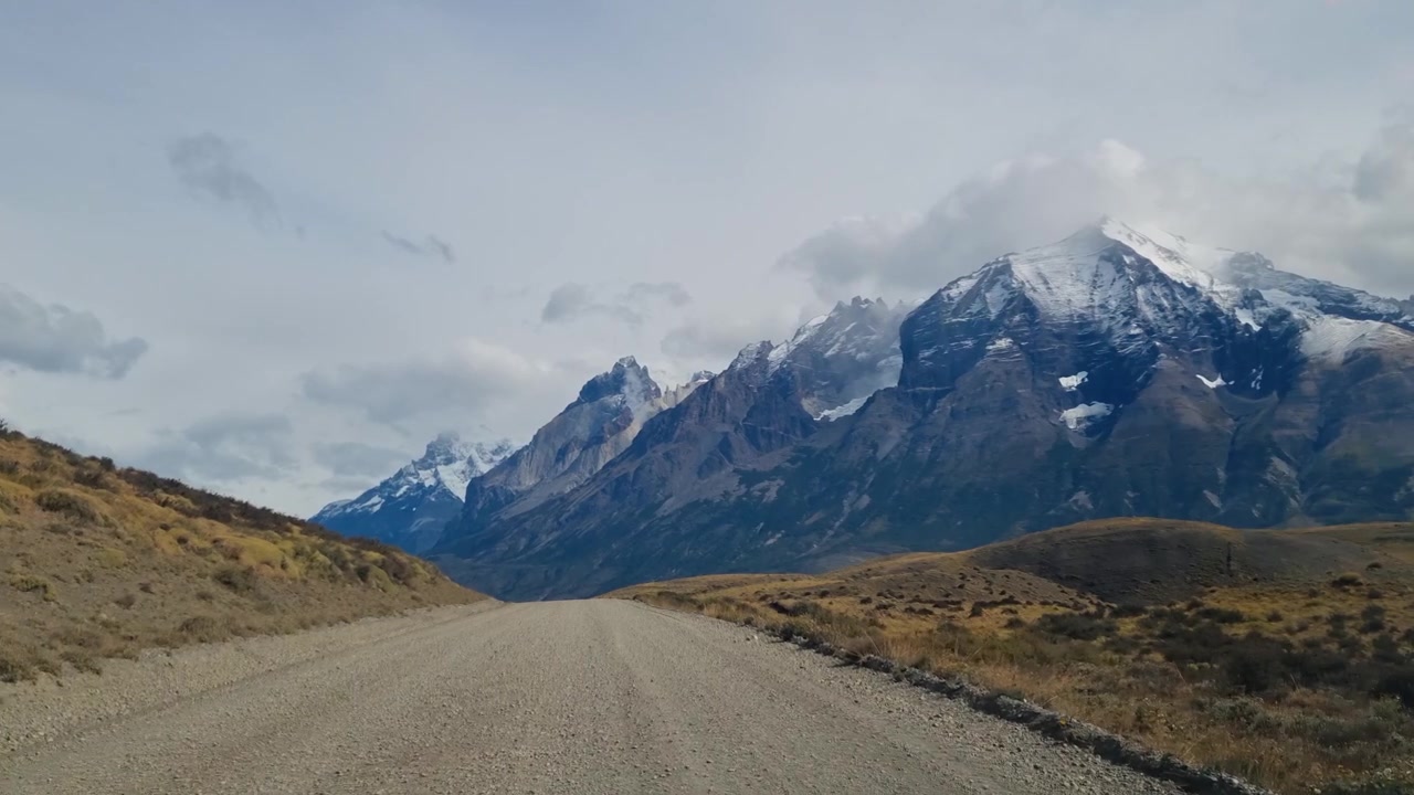 Un viaggio panoramico attraverso la natura selvaggia incontaminata del Parco Nazionale Torres del Paine, Cile, con gli iconici Cuernos del Paine che emergono sotto un cielo nuvoloso e drammatico.