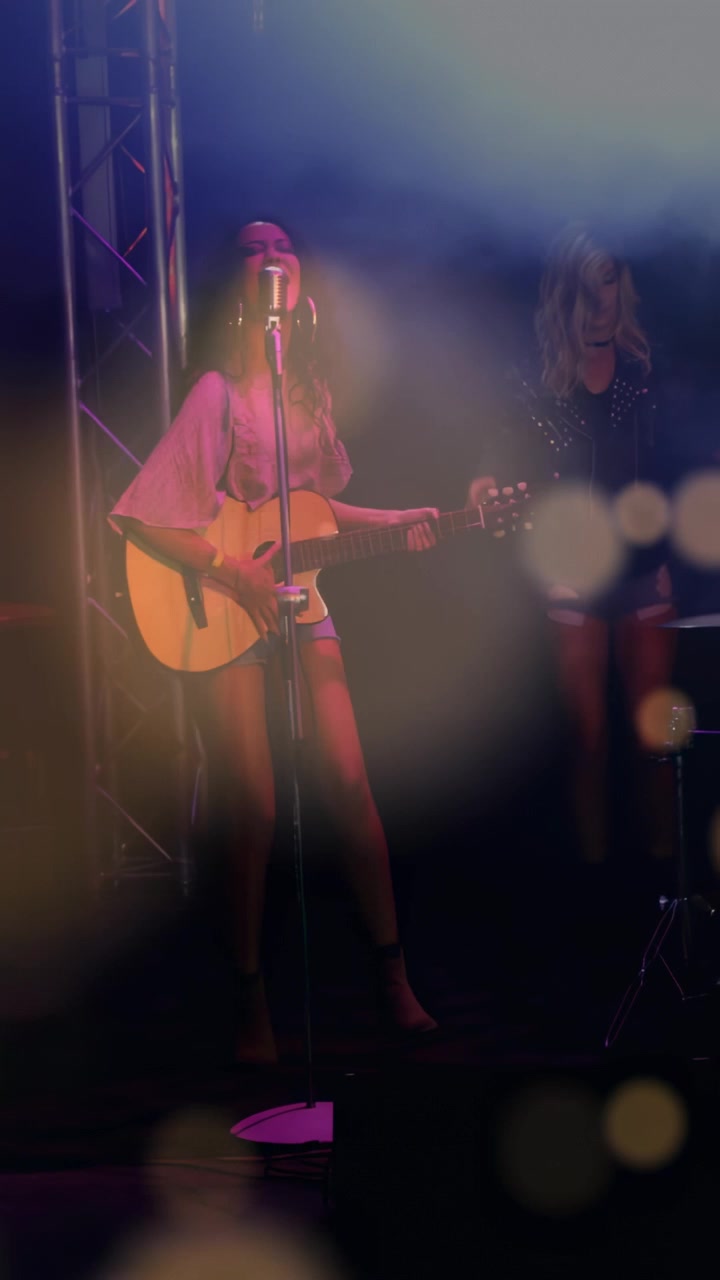 Video vertikal: Penyanyi mulai memetik, menampilkan musik di mikrofon retro sementara lampu kabut menciptakan efek bokeh.