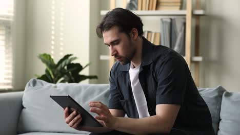 smiling young man sit on sofa use modern digital pad