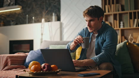 focused freelancer typing laptop sitting couch living room late evening close up