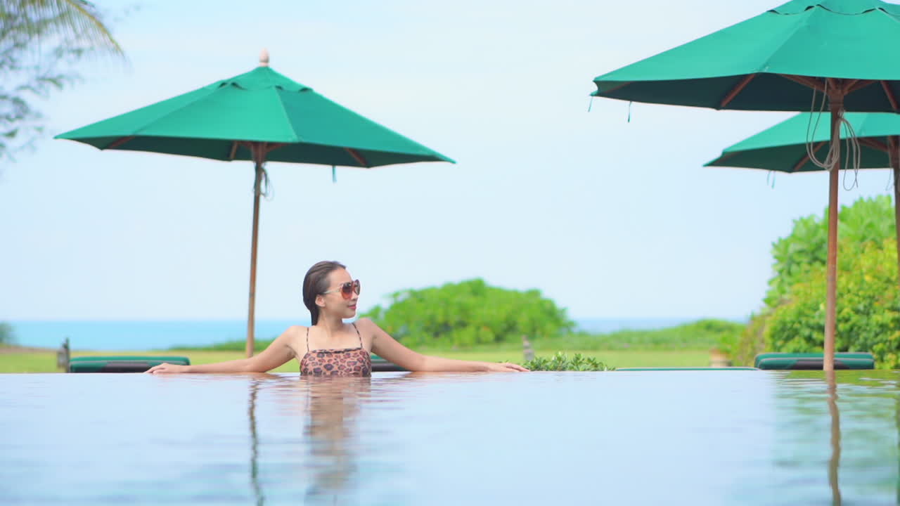 Erwachsene Frau, die allein in einem Hotel-Schwimmbad mit grünen Sonnenschirmen steht.