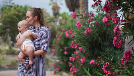 at the resort, amidst palm trees and blooming flowers, a mother engages in a playful display of affection, hugging and kissing her child. this reflects the pure joy of a happy family