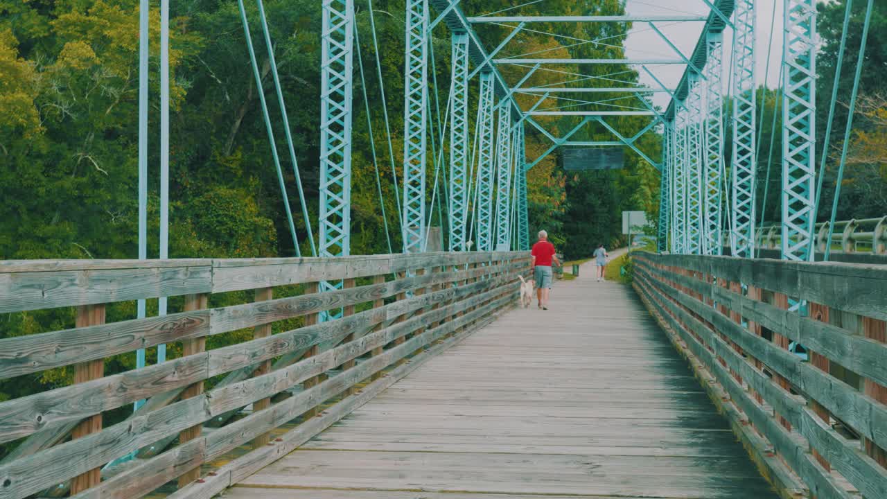안정적으로 흐르는 강 위에 위치한 인도교를 건너는 두 사람과 개