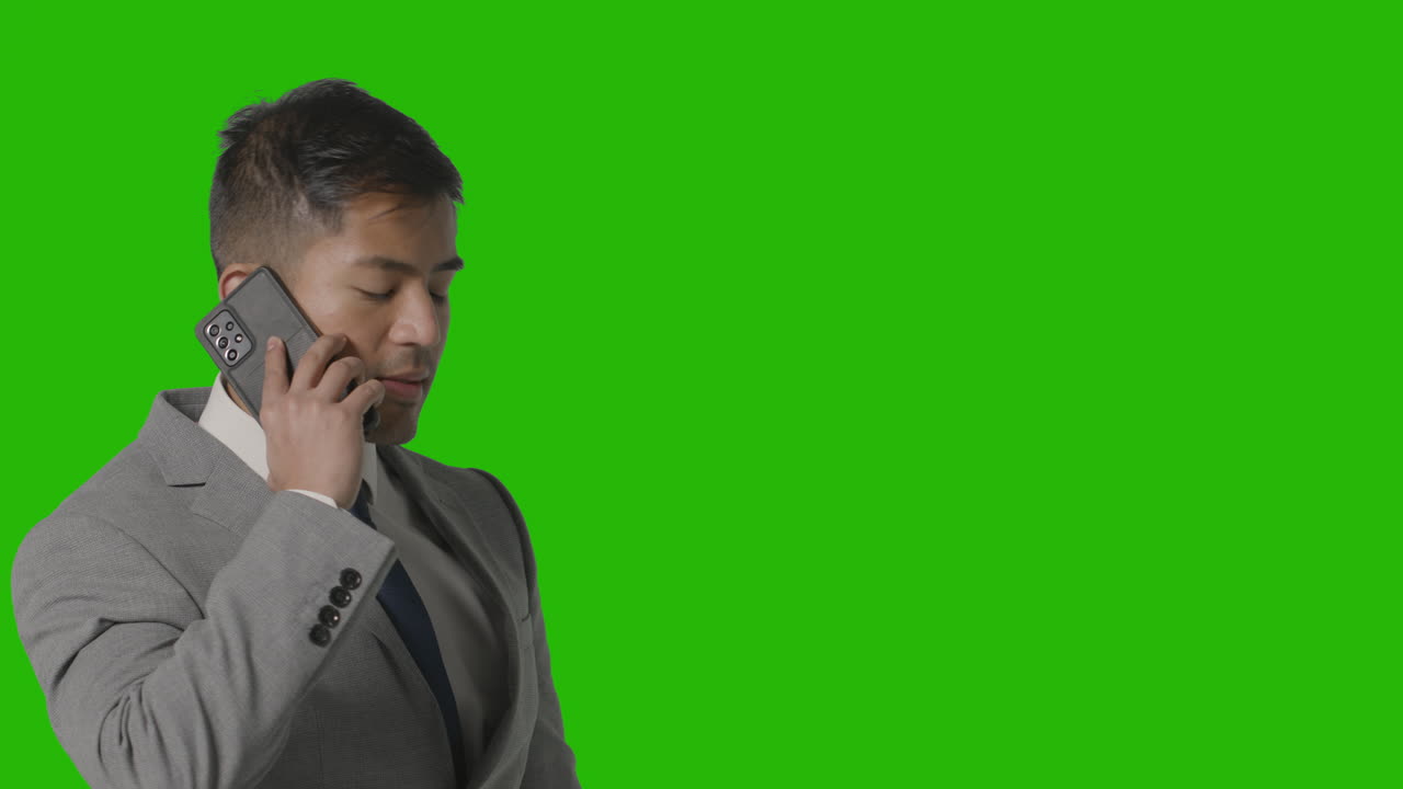 colpo dello studio dell'uomo d'affari serio in vestito che prende chiamata sul telefono cellulare contro lo schermo verde 2