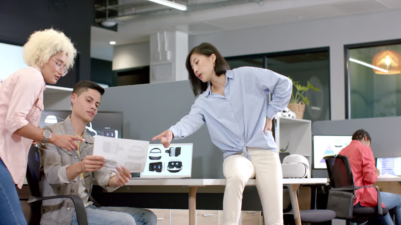 Collaborating in modern office, team discussing VR headset designs, reviewing documents