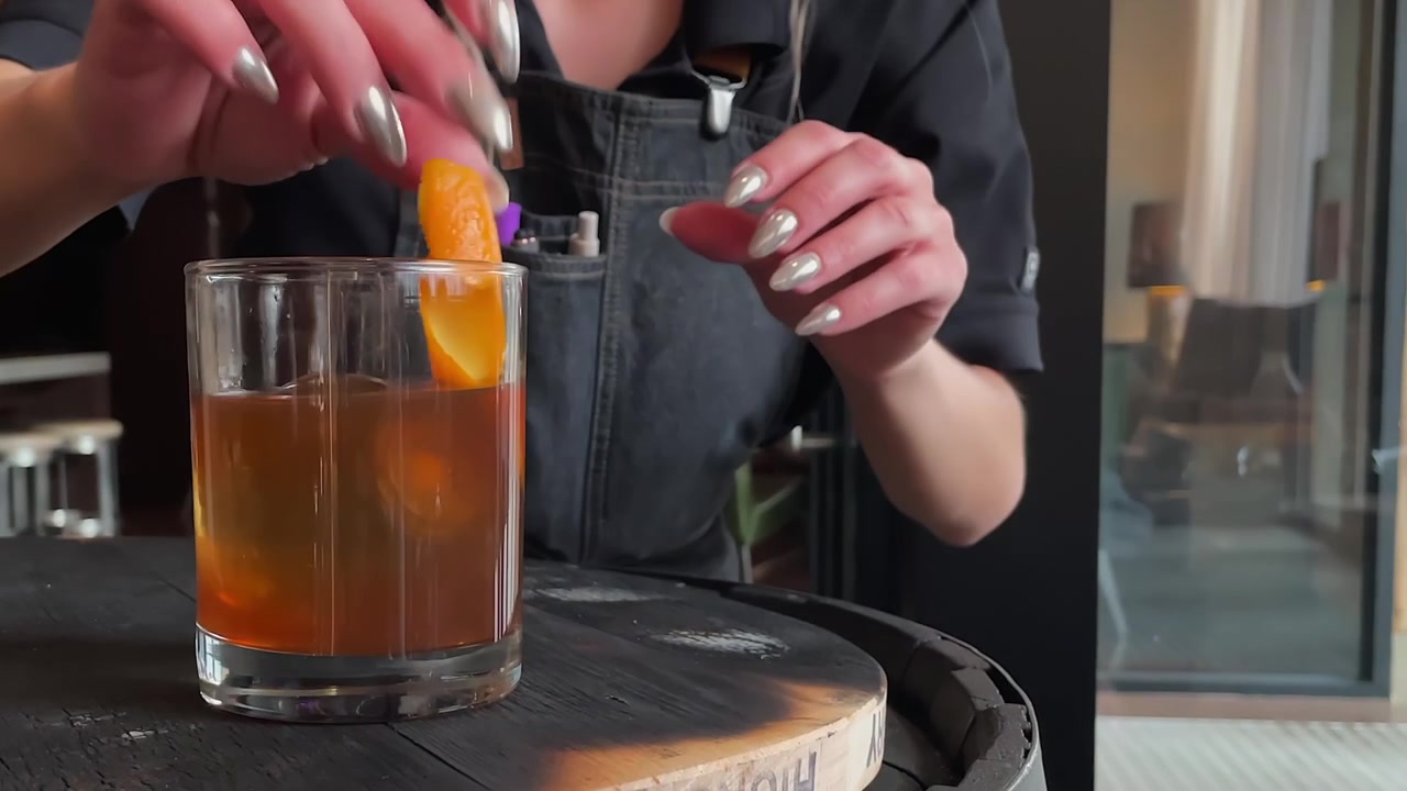 Kvindelig bartender tilføjer et twist af appelsinskal til et glas bourbon-whisky