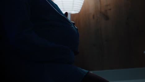 pregnant belly of an unrecognized woman. lady strokes her belly tenderly with love. night lamp is on at backdrop.