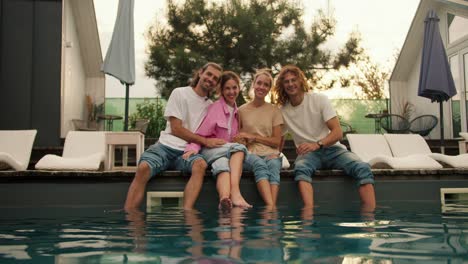 portrait: four friends are sitting near the sunbeds near the sunbeds by the pool and smiling. rest in the country house