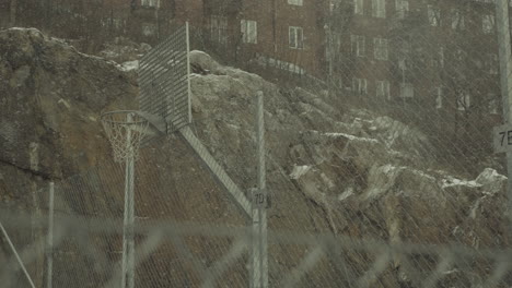 snow falling heavily on an urban metallic basketball court in the suburbs