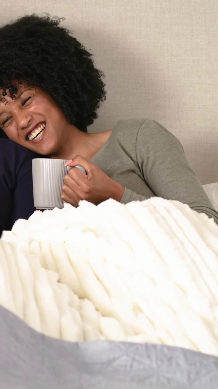 Video verticale: Donna sorridente in top con tazza che si gira mentre un uomo parla con un cappello di Babbo Natale, ridendo a letto