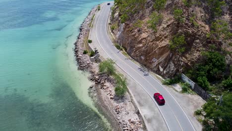 aerial view of traffic driving along coastal road next to crystal clear turquoise ocean water in dili on tropical island of timor-leste, southeast asia