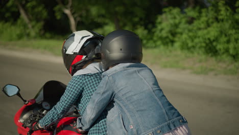 two ladies riding a power bike on a tarred road, wearing helmets, while a jeep passes them on the side, the background includes a blur of grass by the roadside