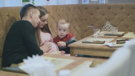 el padre vestido de negro muestra al niño el vientre de la esposa embarazada