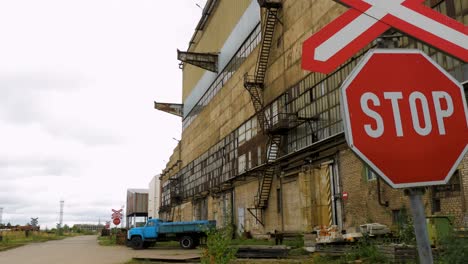 vista exterior de la fábrica soviética abandonada de fundición de metalurgia pesada liepajas metalurgs territorio, señal de alto en los ferrocarriles, camión de carga azul en el fondo, día nublado, plano general