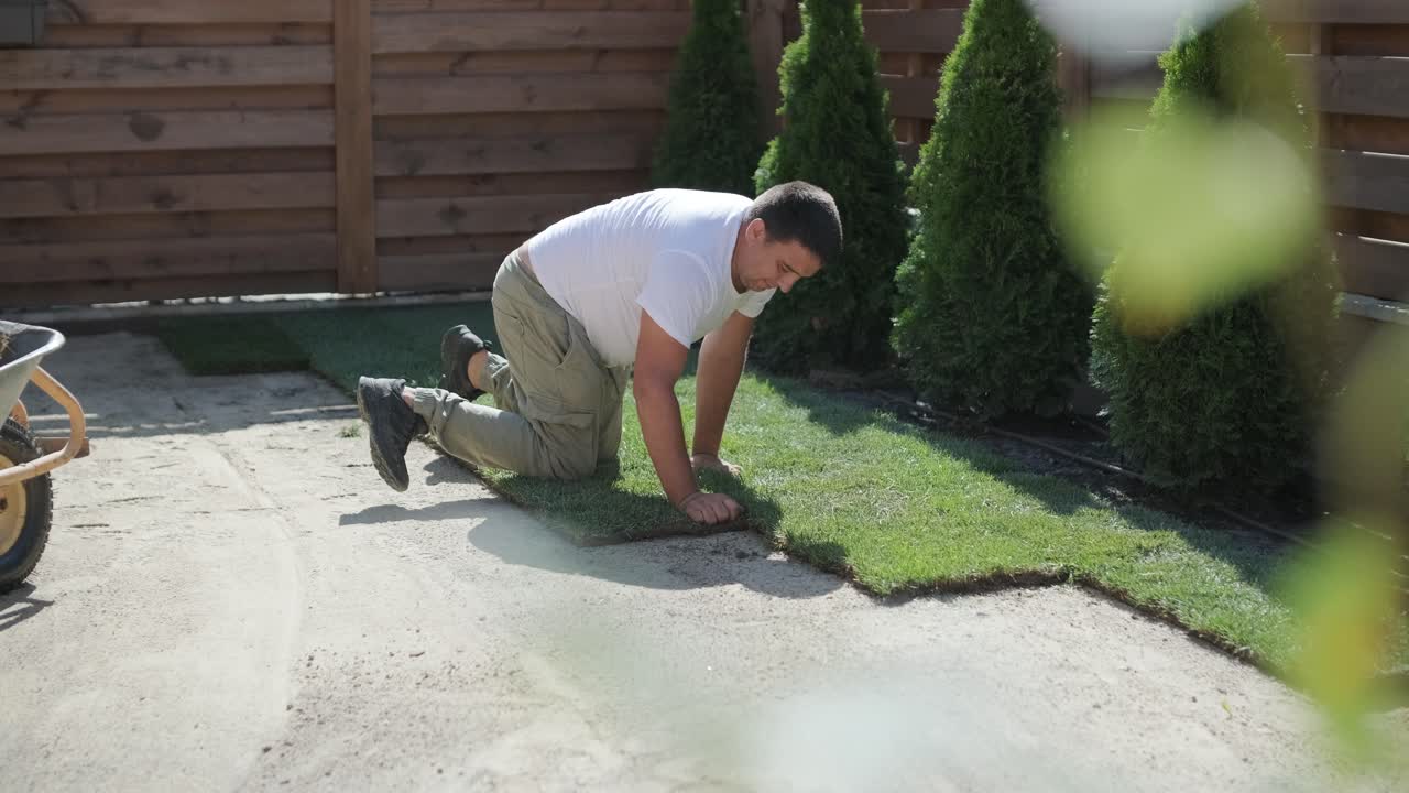 Man Laying Sod Grass in Backyard Garden for Lawn Installation and Landscaping Project, Focused on Home Improvement and Outdoor Maintenance for a Fresh, Green Lawn in a Residential Yard