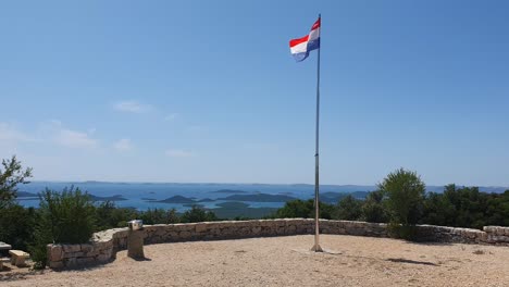 Bandera-Nacional-Croata-Ondeando-En-El-Viento-Con-Tablero-De-Ajedrez-Rojo-Y-Blanco-Con-Hermosas-Vistas-De-La-Costa-Del-Mar-En-El-Fondo