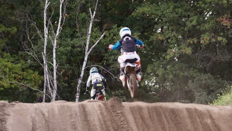 Rückaufnahme-Eines-Motocross-Rennens-Von-Kindern-In-Der-Sprungzone,-Die-über-Den-Hügel-Springen