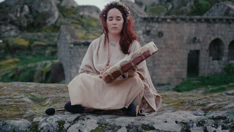 spiritual woman playing a shamanic drum in a beautiful medieval village long shot