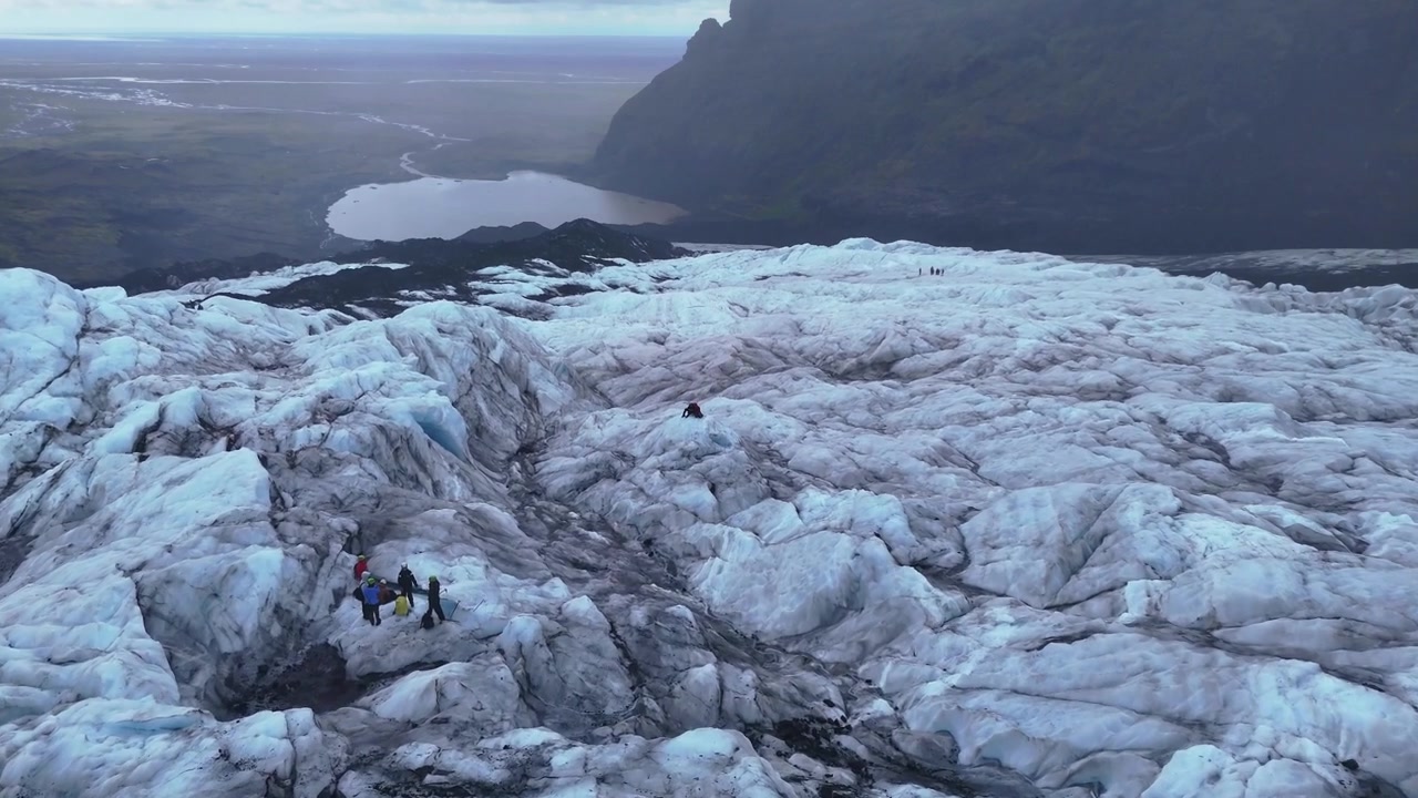 Droneoptagelser der flyver over en islandsk gletsjer under regnvejr med guidede turgrupper, der udforsker det iskolde landskab. Filmisk luftfoto, der viser eventyrturisme, dramatisk natur og ekstrem natur.