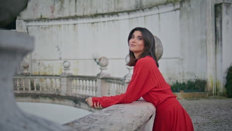 dreamy girl posing fountain standing in city square wearing red dress closeup