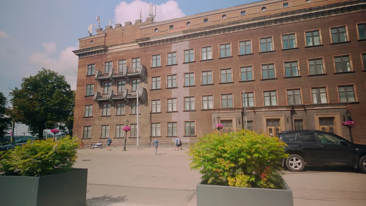 Dolly shot of the exterior of Riga Technical University with students walking by, cars parked, and multiple windows visible. Located in the city center, Riga, Latvia