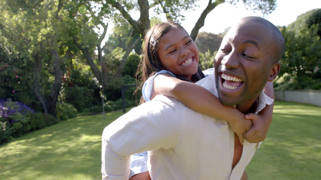 Father giving daughter piggyback ride, both smiling and enjoying outdoor time