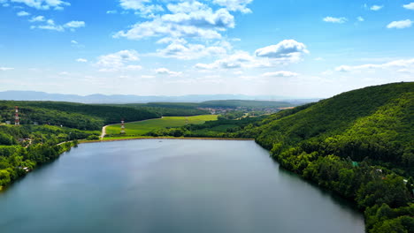 Calm lake by green hills in Europe. A tranquil lake lies nestled between lush green hills, reflecting the blue sky and inviting nature lovers to explore