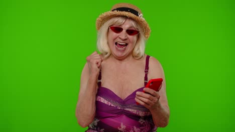 mujer madura viajera navegando en el teléfono móvil y celebrando ganando vacaciones en el complejo turístico