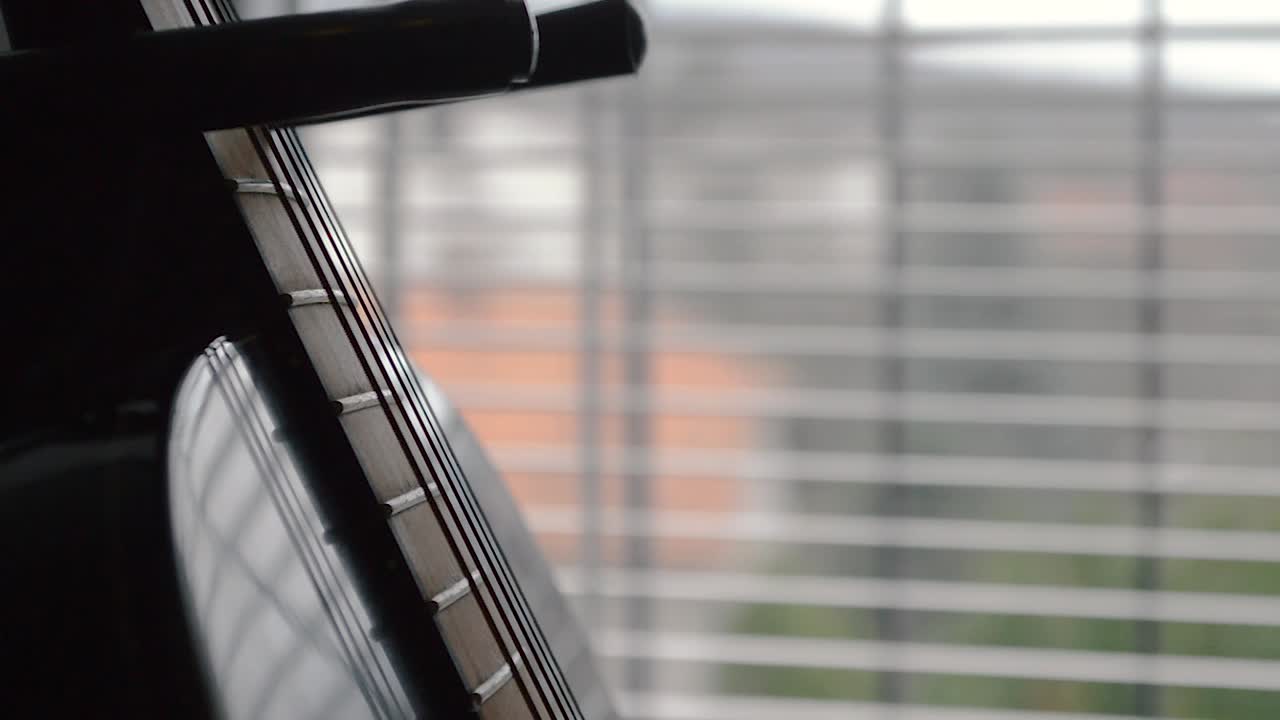 Strings and fretboard of a black guitar on a stand by the window