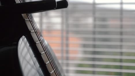 strings and fretboard of a black guitar on a stand by the window