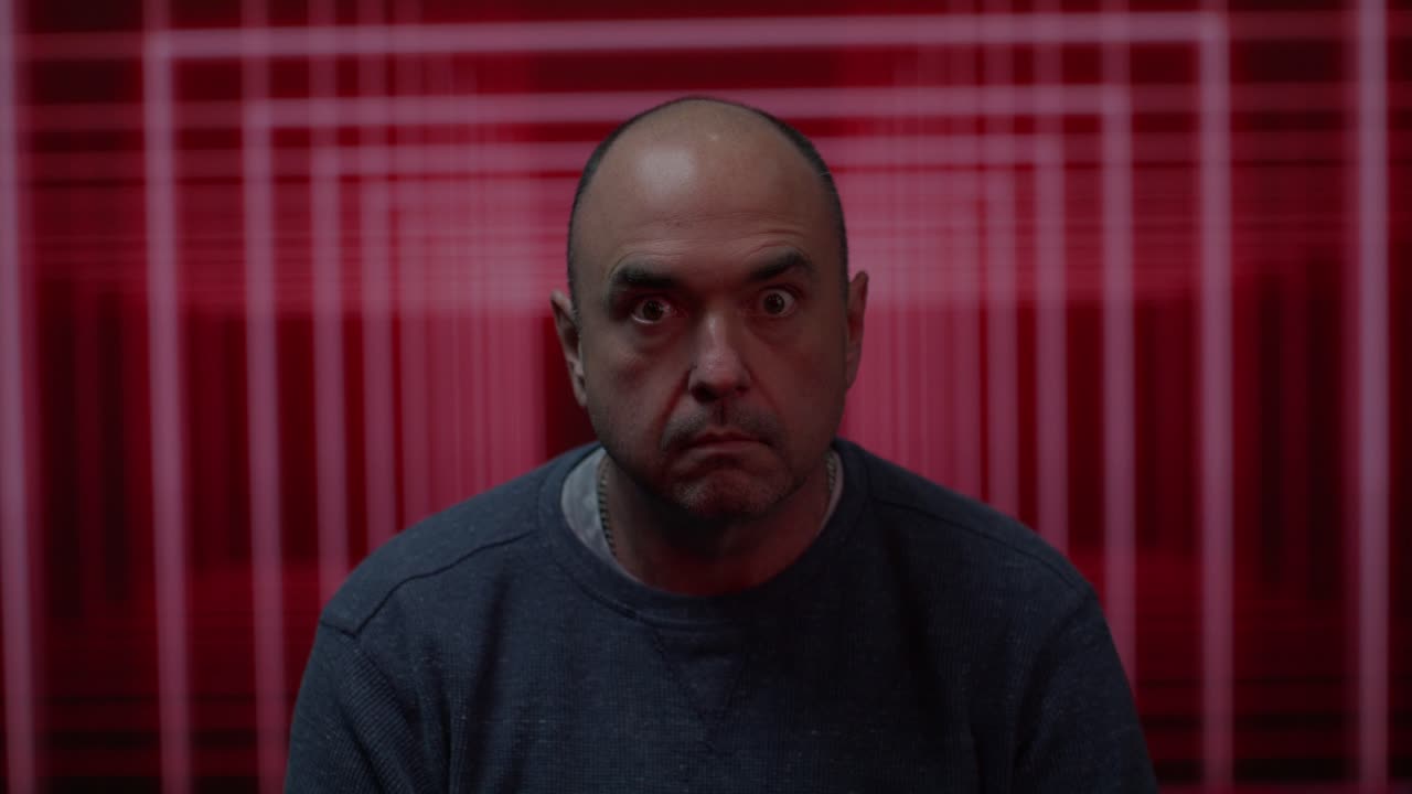 hombre blanco de mediana edad mirando hacia la cámara con un fondo colorido en movimiento