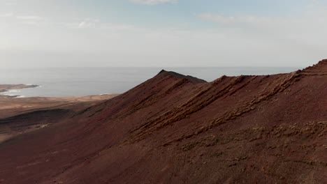 pull back drone shot of a red volcano by the ocean