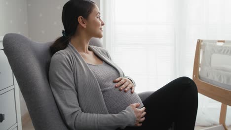 zoom in of caucasian woman in advanced pregnancy sitting on armchair and stroking the abdomen.