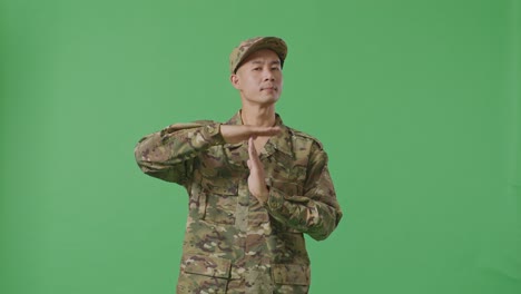 asian man soldier looking at camera and showing time out hands gesture while standing in the green screen background studio